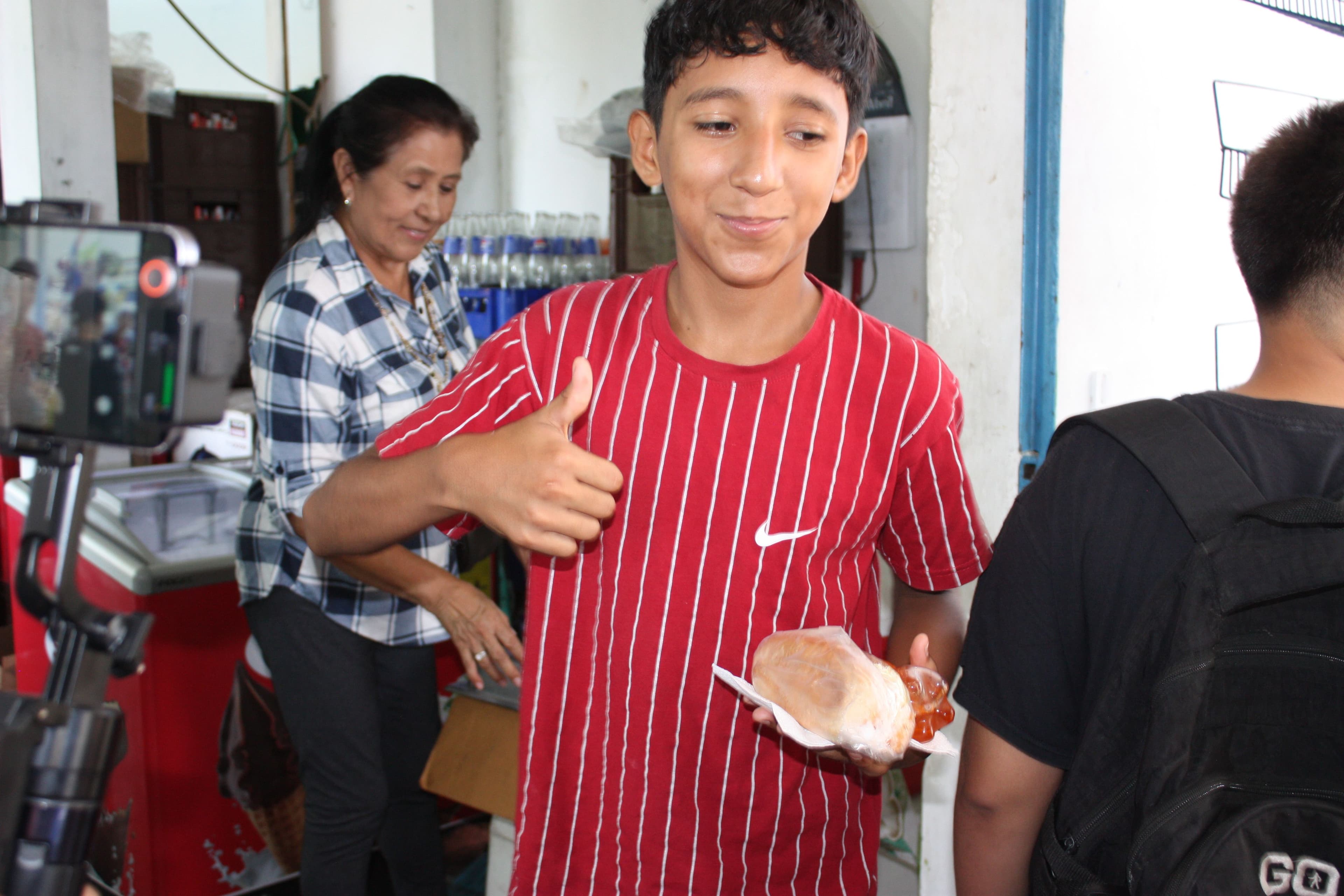 Kid in red shirt smiling with sandwich in hand
